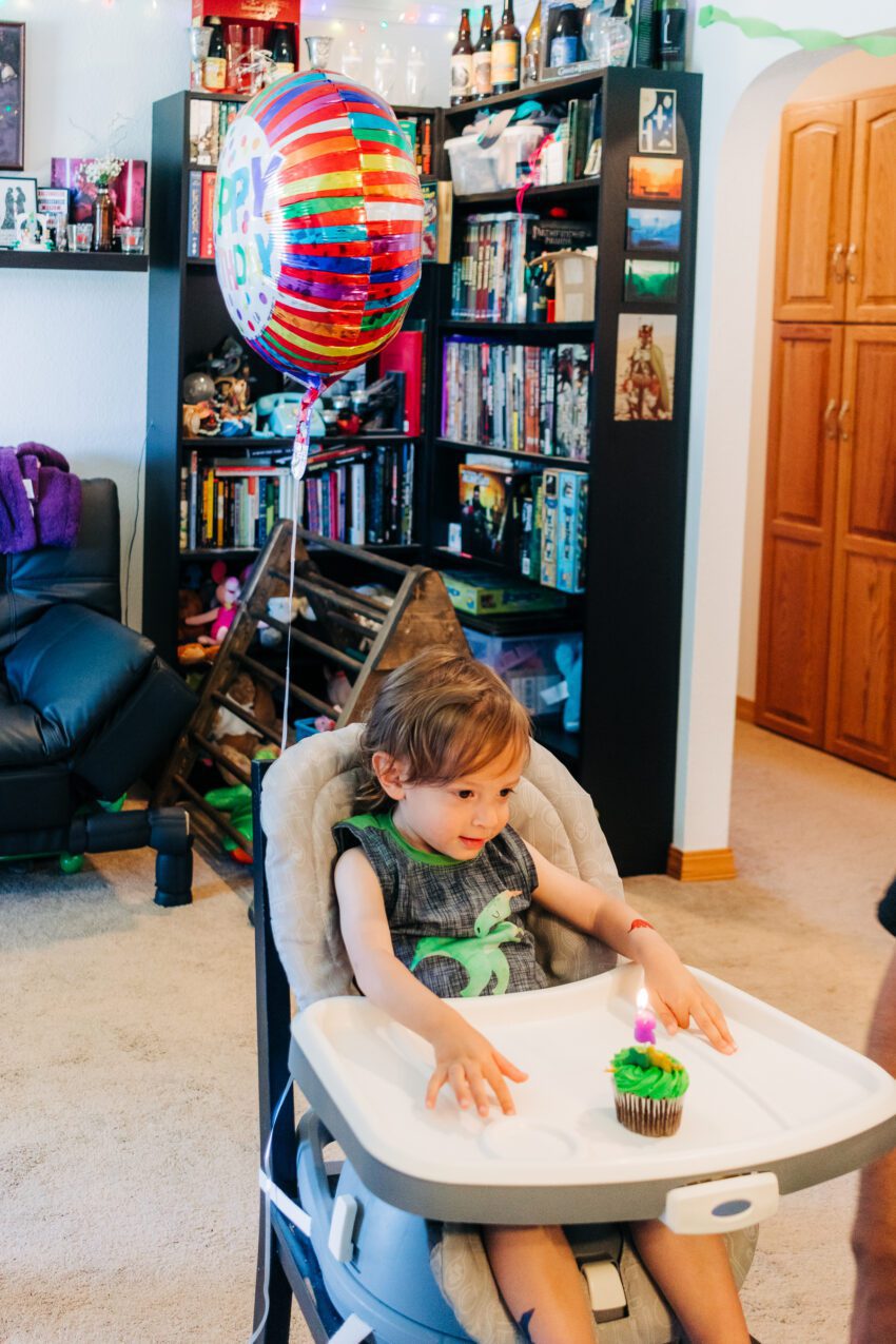 A two year old in a dinosaur tank top with a cupcake